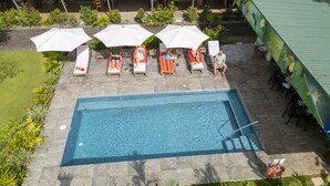 An outdoor swimming pool with lounge chairs and umbrellas, surrounded by greenery and a building with a green roof. - Paradiselodge - Romantic Hideaway, next to Nauyaca (Platanillo de Baru)