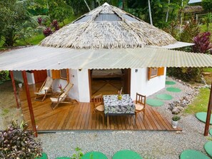 A thatched-roof hut with a wooden deck, a table with chairs, and a small garden area. - Paradiselodge - Romantic Hideaway, next to Nauyaca (Platanillo de Baru)