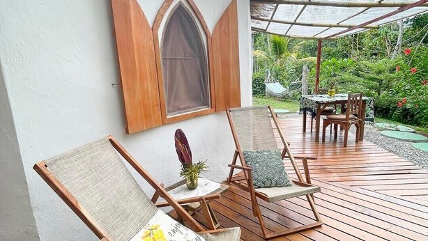 A wooden deck with a covered seating area, a table, and a view of a garden. - Paradiselodge - Romantic Hideaway, next to Nauyaca (Platanillo de Baru)