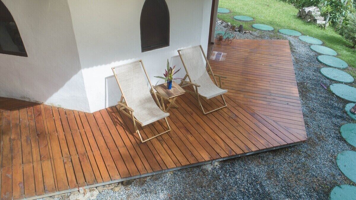 Una terraza de madera con dos sillas reclinables y una mesita con una planta.