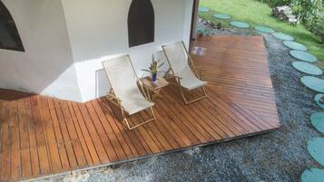 Una terraza de madera con dos sillas reclinables y una mesita con una planta.