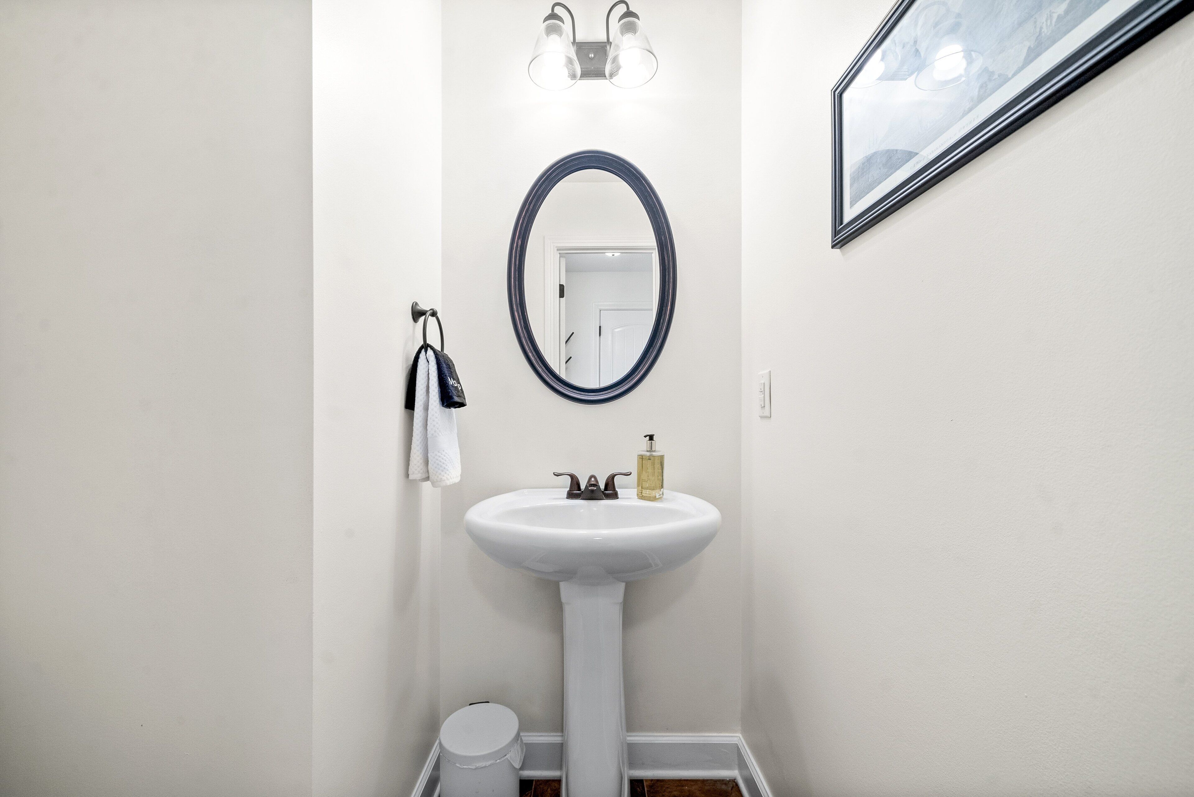 A bathroom with a white pedestal sink, a round mirror, and a wall-mounted light fixture.