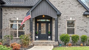 A brick house with a dark front door, two small windows, and a porch with steps.