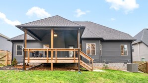 A residential house with a covered porch, a brick foundation, and a grey exterior.