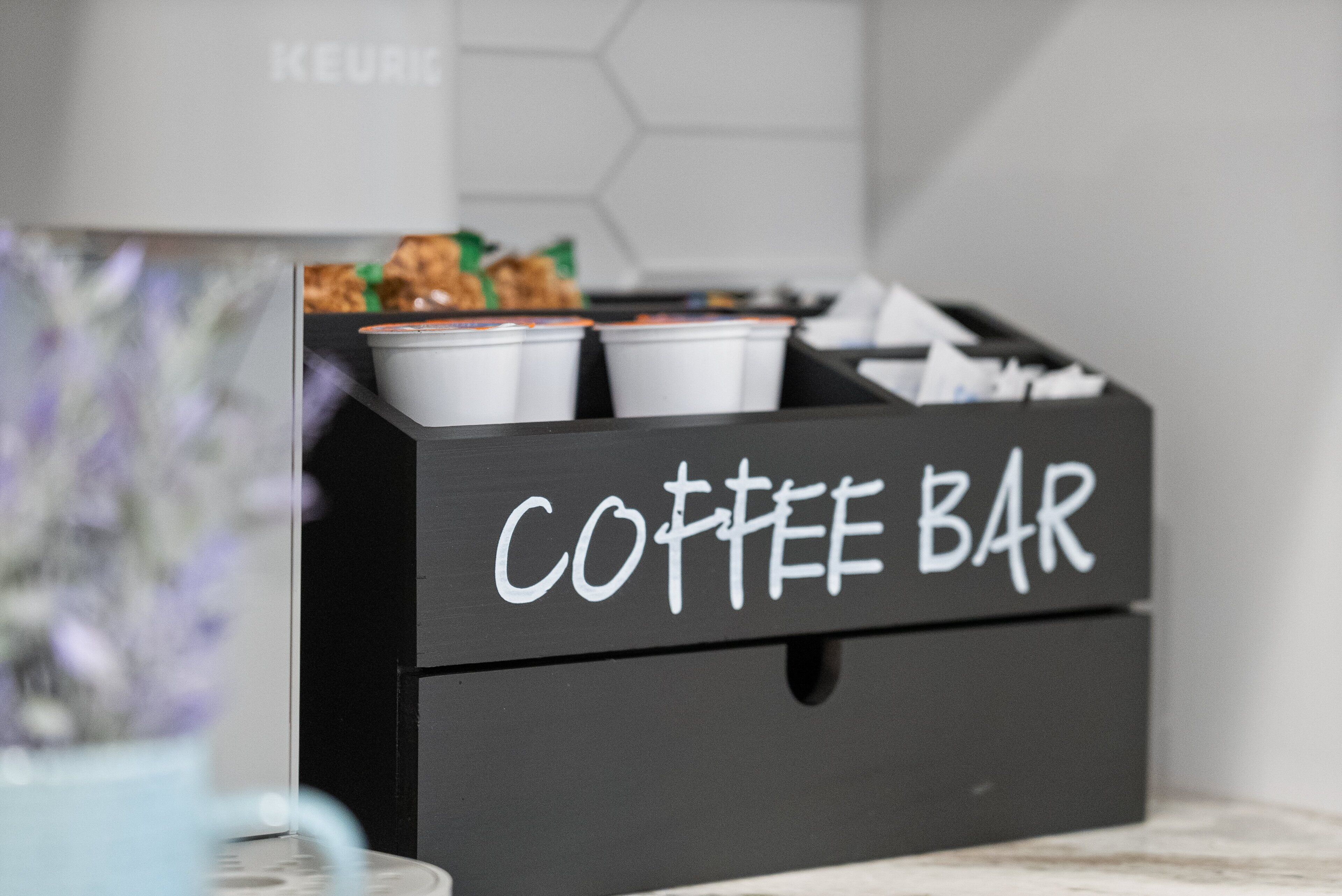 Une boîte de rangement noire portant l’inscription « BAR À CAFÉ » et contenant plusieurs tasses blanches.