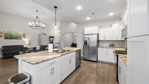 A modern kitchen with white cabinetry, a central island, stainless steel appliances, and a dining area with a dark sofa and lamp.