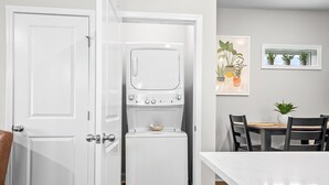A compact kitchen with a built-in washer and dryer, a dining table with chairs, and a potted plant on the wall.