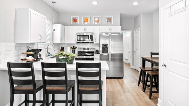 Une cuisine moderne avec des meubles blancs, des appareils en acier inoxydable et des chaises à rayures noires.