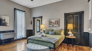 Une chambre à coucher comprenant un lit, des tables de chevet, un bureau, une chaise et une fenêtre avec des rideaux.