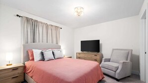 A bedroom with a bed, a TV, a chair, and a nightstand. - Loft #210 (540 N 2nd St) (Fredericton)