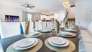 A dining area with a long table set for multiple guests, featuring woven placemats, white plates, and clear glassware. - Special Offer! Lake View/Themed BR/Pool/SPA 22093 (Kissimmee)