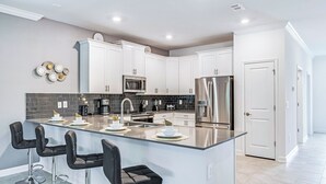 A modern kitchen with white cabinets, a stainless steel refrigerator, a microwave, and a large island with bar stools. - Special Offer! Lake View/Themed BR/Pool/SPA 22093 (Kissimmee)
