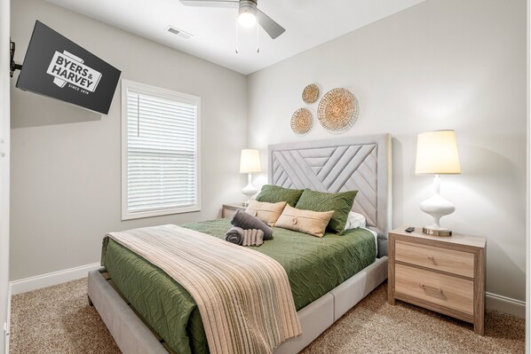 A bedroom with a bed, nightstands, a TV, and wall decor.