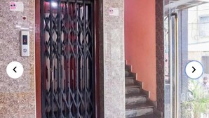 Une entrée d’immeuble avec un portail en métal, un escalier et une porte vitrée donnant sur un balcon où se trouve un pot de fleurs.