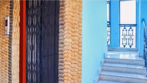 Un bâtiment en pierre avec une porte noire et un escalier bleu doté de rampes en métal.