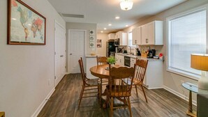 A compact kitchen with white cabinets, a dining table with chairs, a globe map on the wall, and a window with blinds.