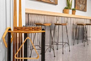 Une rangée de tabourets de bar avec un plateau supérieur en osier, des pieds en métal et un comptoir en bois agrémenté de plantes.
