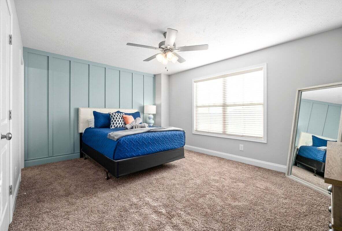 Ein Schlafzimmer mit Bett, Deckenventilator, Fenster mit Jalousien und Spiegel.