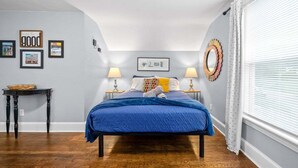 A bedroom with a bed, two bedside lamps, a small table, and a wall with framed pictures.