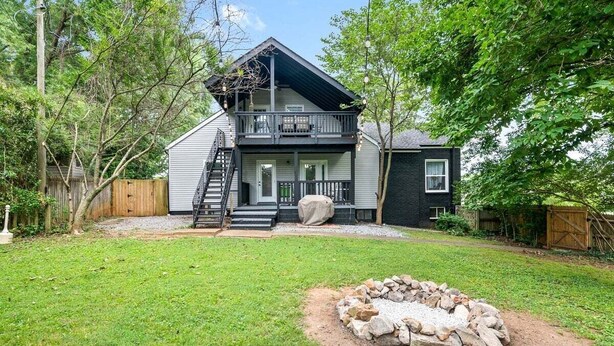 A two-story house with a balcony, a front porch, and a stone fire pit in the yard.