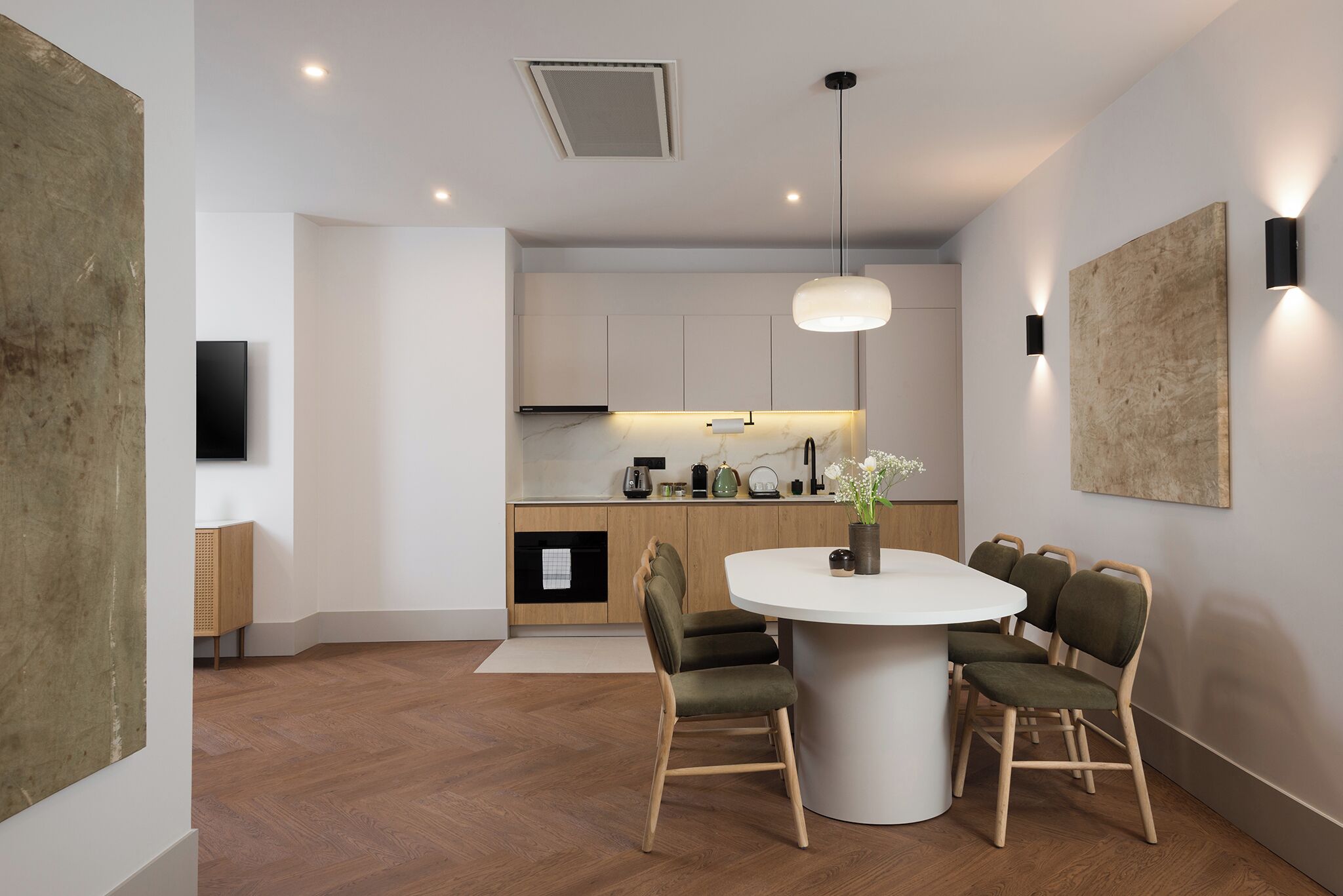 A modern kitchen with a round dining table, wooden cabinets, and pendant lighting.