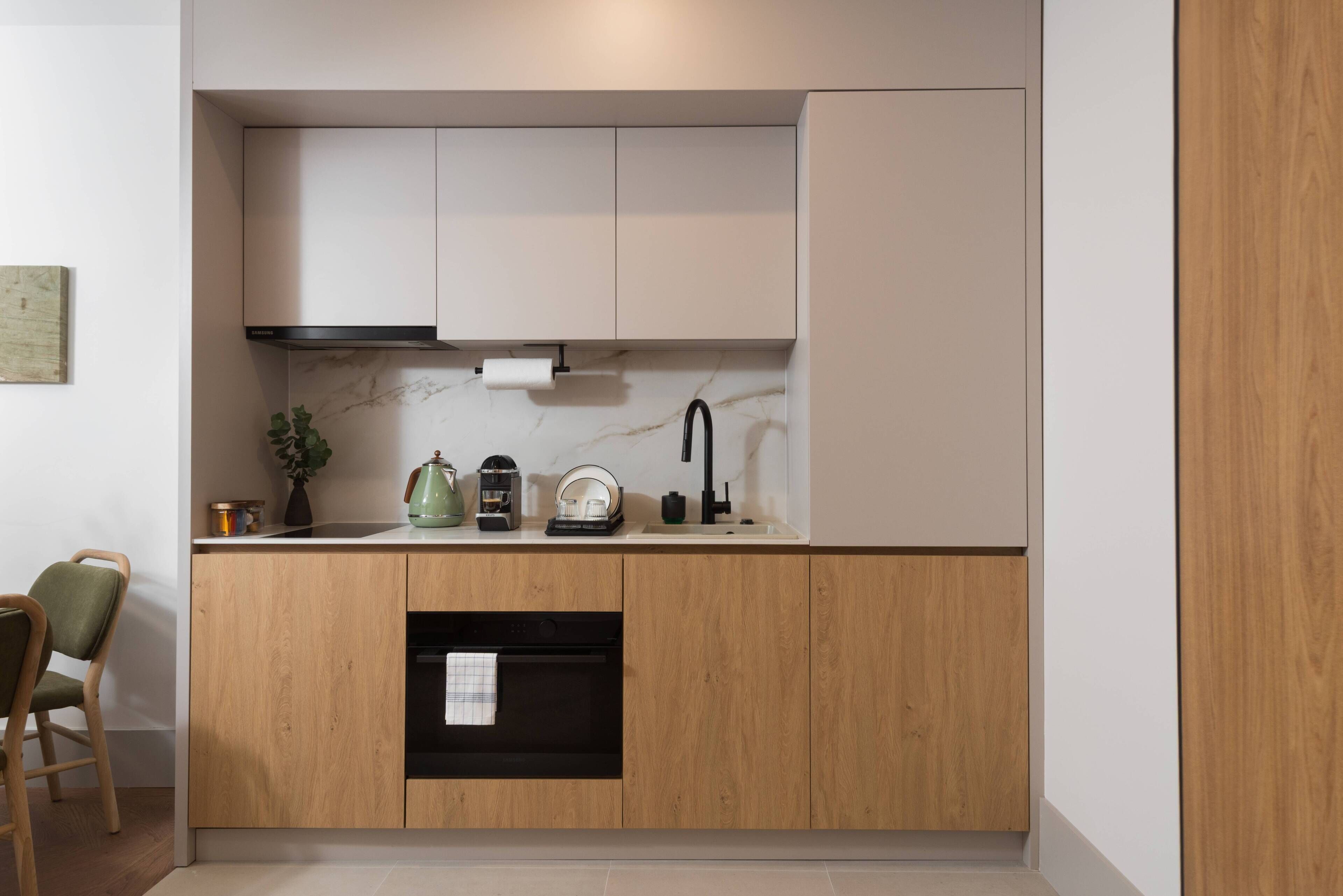 A compact kitchen with wooden cabinets, a built-in oven, a sink, and a marble backsplash.