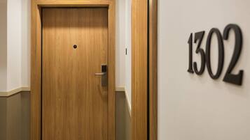 Una puerta de madera con un pomo y un pequeño agujero en el centro. A la derecha de la puerta, se ve un letrero en la pared con el número "1302".