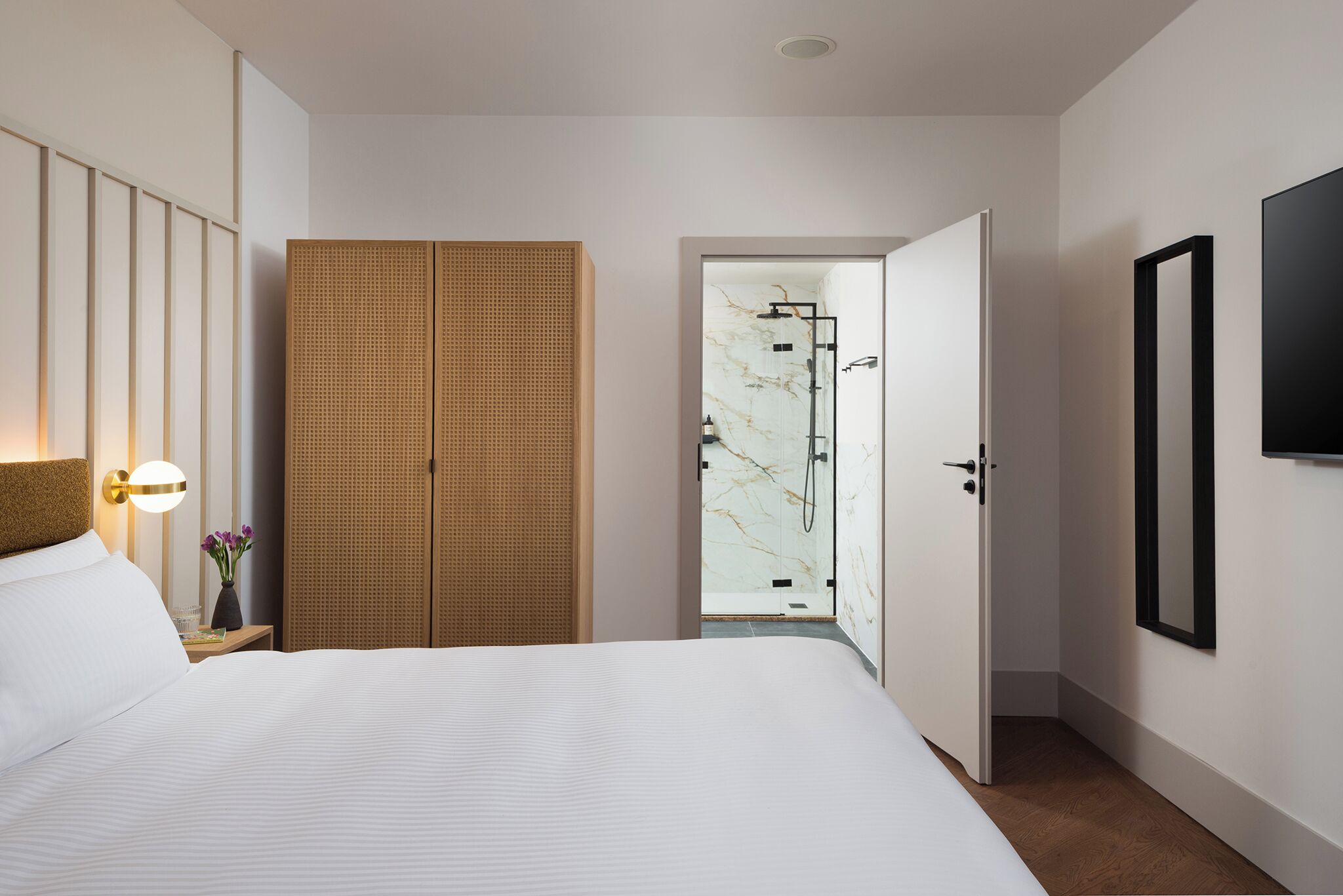 Una camera d'albergo con un letto grande, un armadio in legno, un bagno con doccia in vetro e una TV a parete.