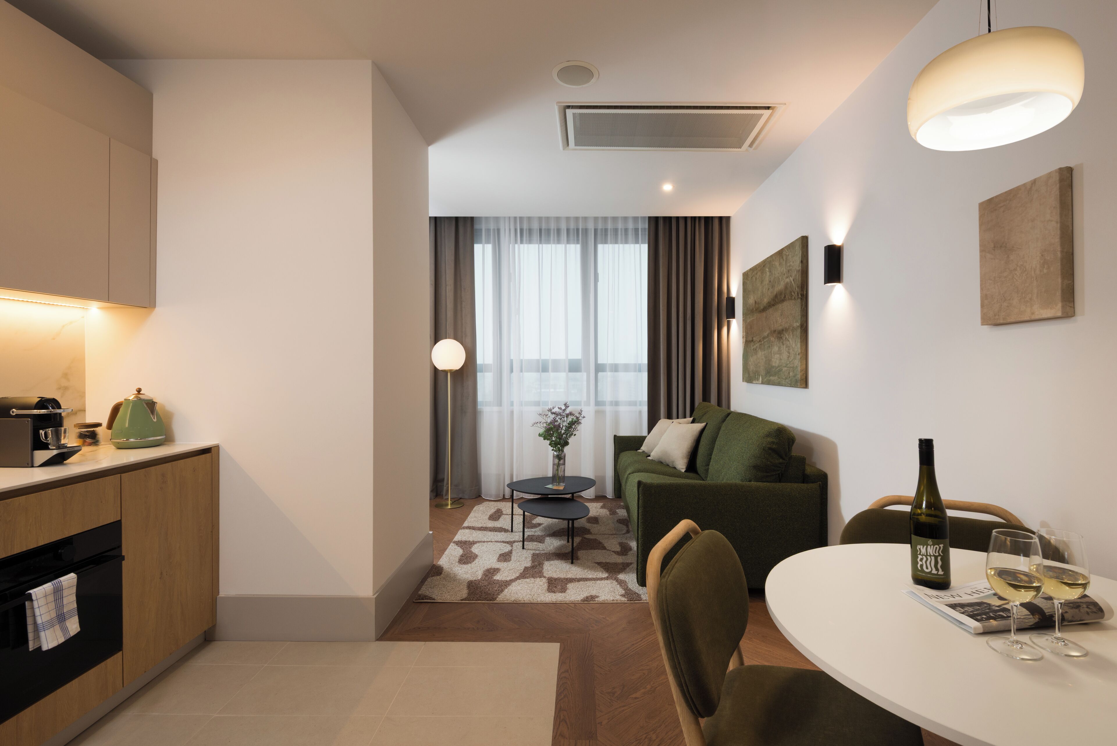 A modern hotel room with a kitchenette, a dining area, and a living space.