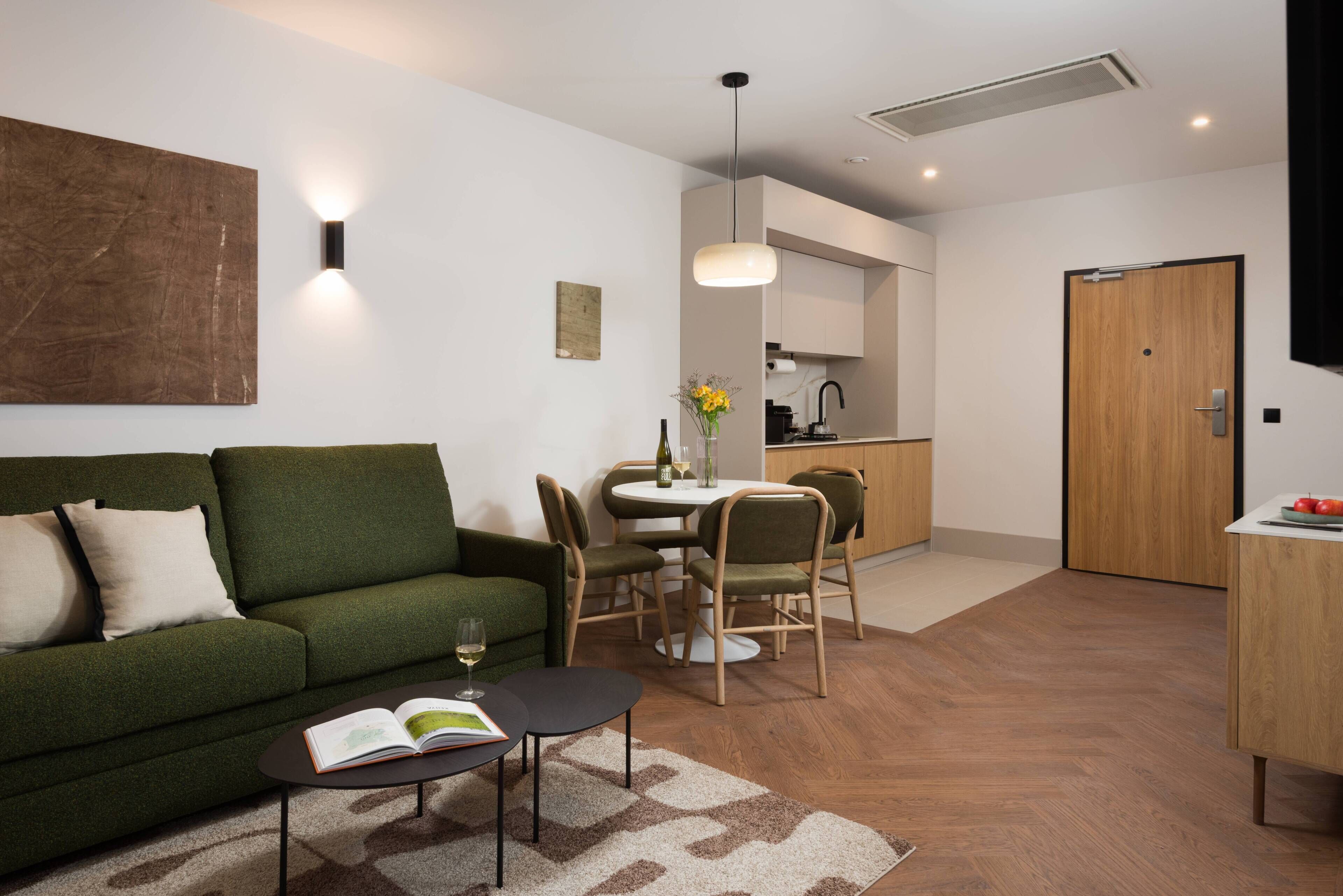 A modern living room with a green sofa, a coffee table with a book, and a dining area with chairs and a table.
