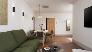 Una sala moderna con un sofá verde, un comedor con mesa y sillas blancas, una puerta de madera y un televisor montado.