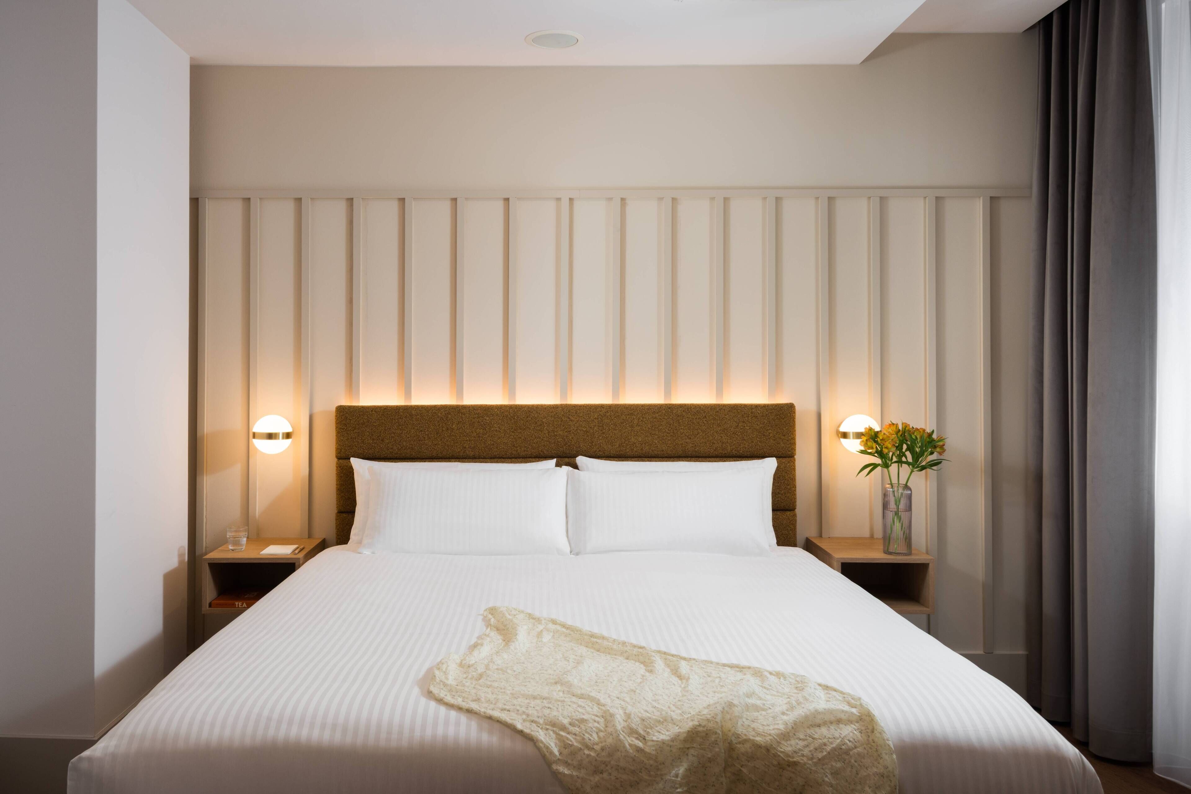 Ein Hotelzimmer mit einem großen Bett, zwei Nachttischen, einem Kopfteil und einem Beistelltisch mit Blumen.