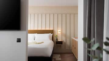 A modern hotel room with a large bed, a bedside table with a lamp, a TV mounted on the wall, and a wardrobe.