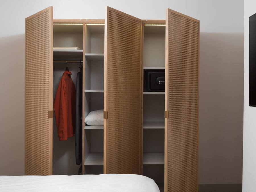 Una habitación con una cama, un armario abierto y un televisor en la pared.