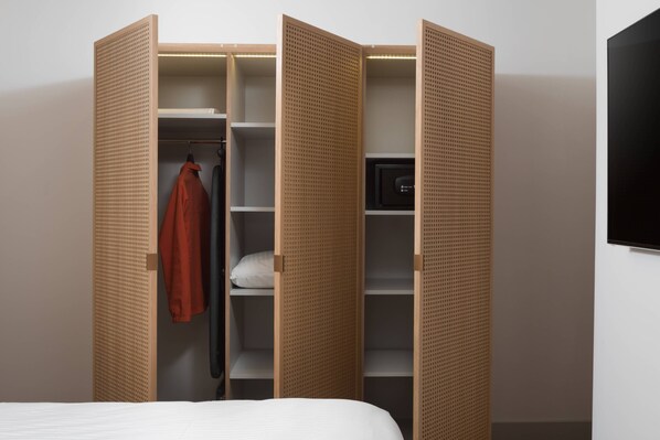 Una habitación con una cama, un armario abierto y un televisor en la pared.