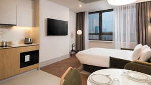 A modern hotel room with a bed, a dining area with a table set for two, a kitchen area with a stove and a television mounted on the wall. - master Wola (Warsaw)