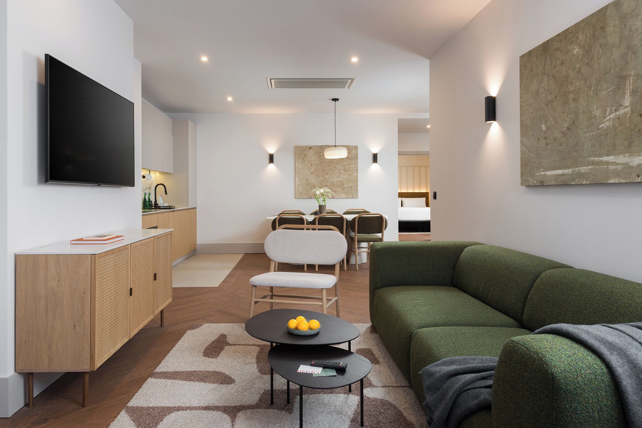 A modern living room with a green sofa, a flat-screen TV, a wooden cabinet, and a dining area with chairs and a table.