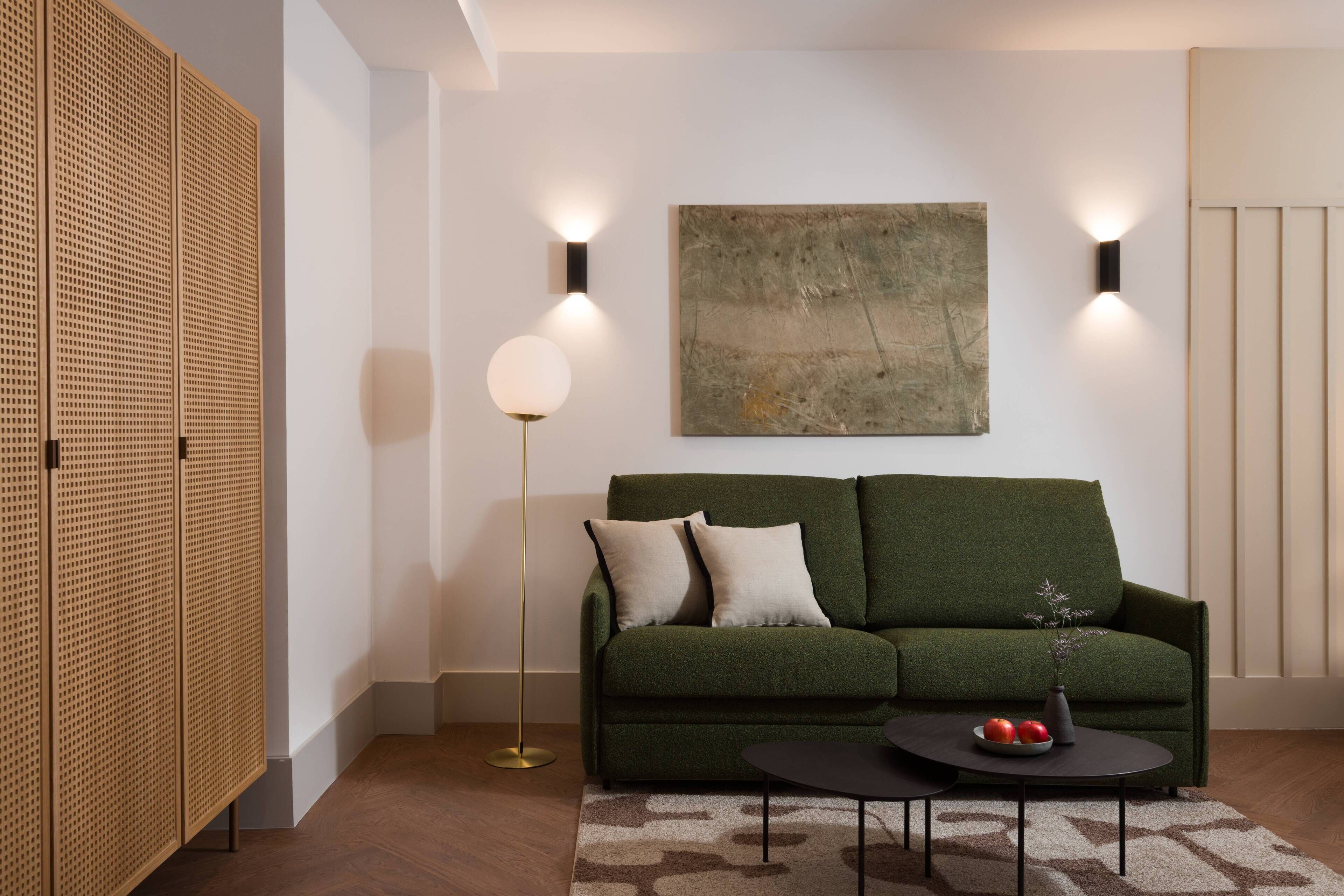 Een moderne woonkamer met een groene bank, een ronde salontafel met fruit, en een groot abstract schilderij aan de muur.