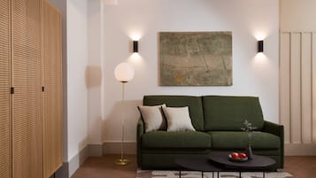 Een moderne woonkamer met een groene bank, een ronde salontafel met fruit, en een groot abstract schilderij aan de muur.