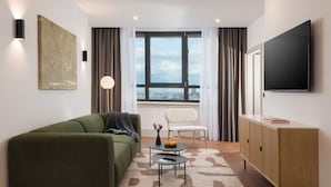 A modern living room with a green sofa, a small round table, a white chair, a TV, and a large window with curtains. - master Wola (Warsaw)