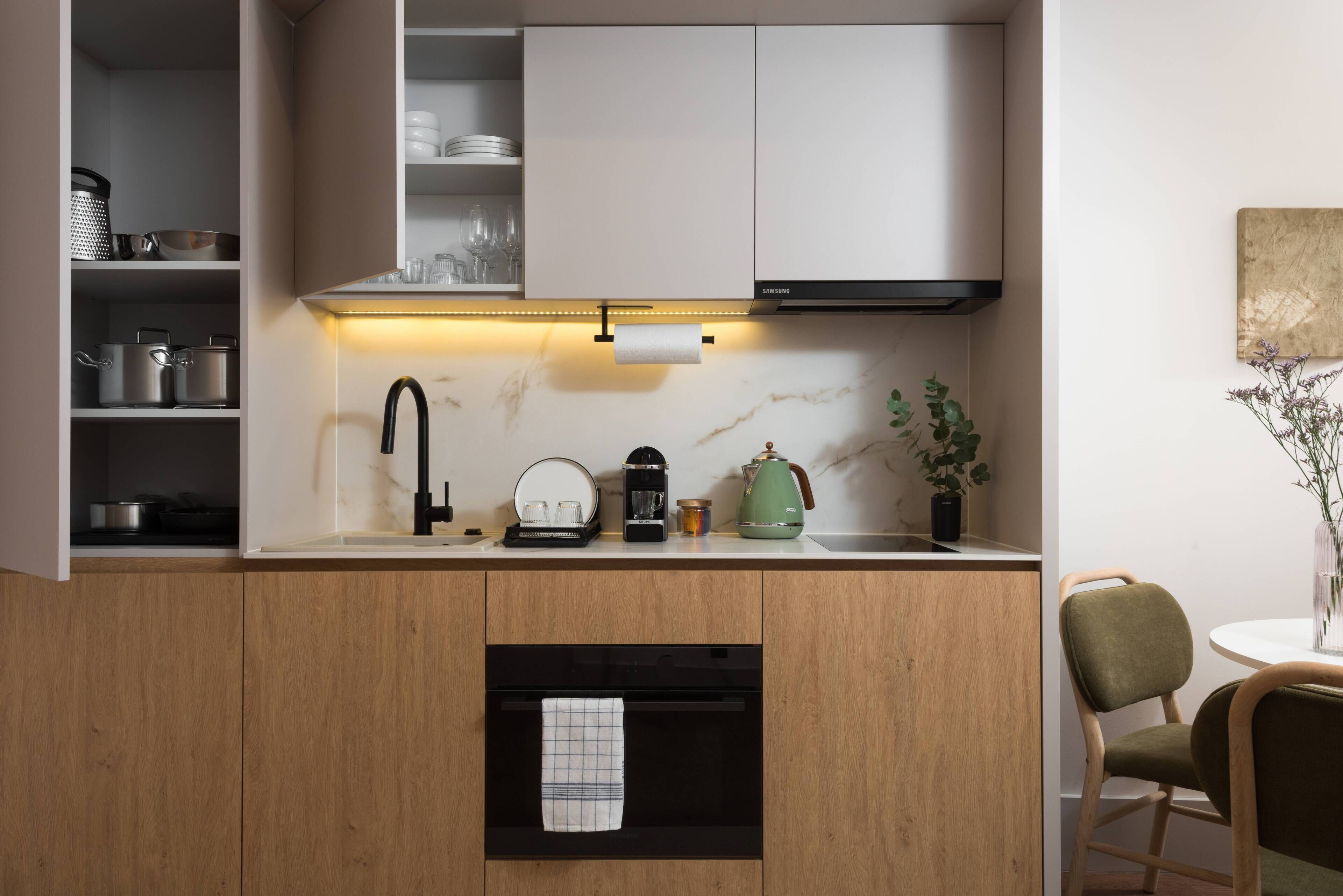 A modern kitchen with wooden cabinets, a built-in oven, a coffee maker, and a green kettle.