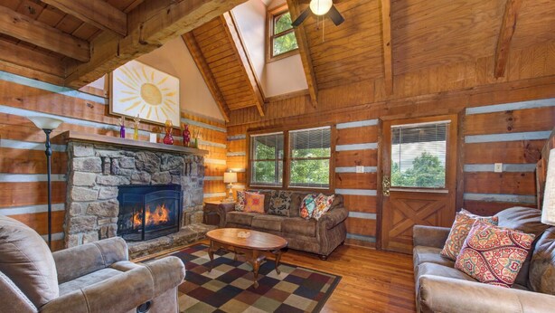 A log cabin interior with a stone fireplace, wooden ceiling beams, and a cozy seating area with sofas and a coffee table.