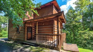 A rustic log cabin with a porch, a front door, and a small set of stairs leading up to the entrance.