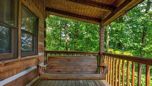 A wooden deck with a bench, surrounded by trees.