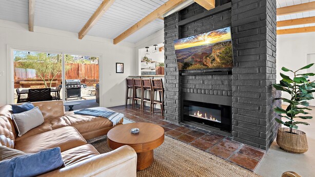 A living room with a stone fireplace, leather sofa, and a dining area with chairs. - Pool•Hot Tub•Firepit•Fully Fenced with Epic Views (Joshua Tree)