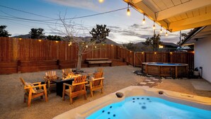 A backyard with a hot tub, wooden chairs, and a table under string lights. - Pool•Hot Tub•Firepit•Fully Fenced with Epic Views (Joshua Tree)