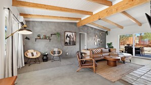 A spacious living area with a high ceiling, exposed wooden beams, a large sofa, a coffee table, and a dining area with a striped rug. - Pool•Hot Tub•Firepit•Fully Fenced with Epic Views (Joshua Tree)