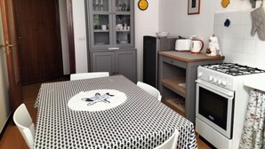 A compact kitchen with a dining table, a built-in oven, a microwave, and a cabinet with glass doors. - Gianlu' Cosy Apartment with A/C (Monterosso al Mare)