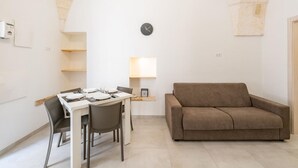 Spiseplads med et bord dækket til to, en sofa, et ur på væggen og en lampe.