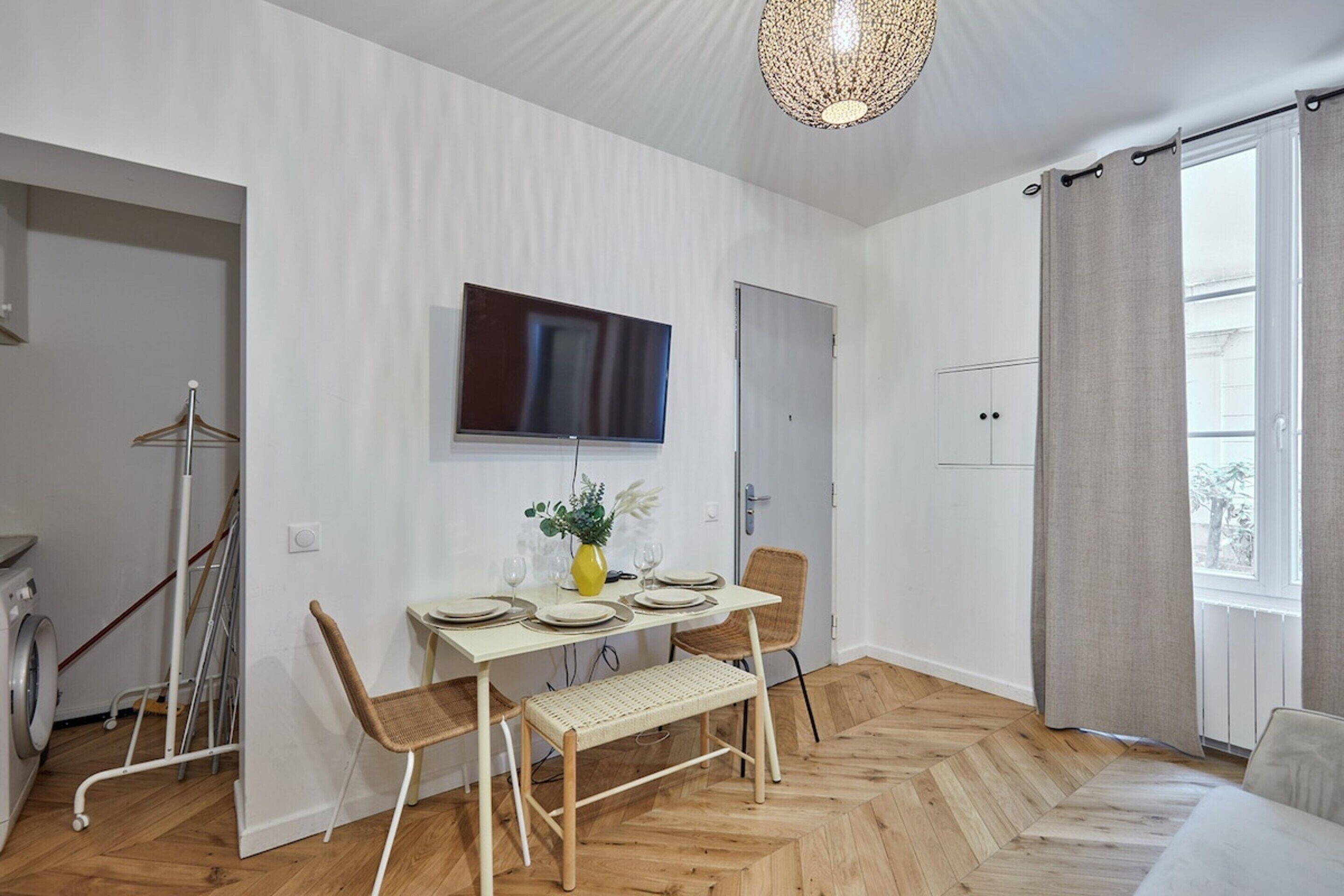 Une pièce moderne comprenant une table à manger, des chaises, un téléviseur fixé au mur et une fenêtre avec des rideaux.